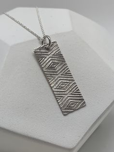 This modern Art Deco style vertical bar necklace has been entirely handmade using .999 fine silver.  It has been cut out from fine silver precious metal clay, textured, fired and oxidized. The pendant hangs from a sterling silver diamond cut cable chain. This fine silver pendant features an embossed Art Deco style diamond textured pattern. Pendant size: approximately 1 1/4 x 3/8 inches Chain length: adjustable at 16 and 18 inches                           can also be customized to whatever length needed The necklace is sent in a gift box.  This jewelry can be used as a gift for Christmas, birthday, anniversary and many other occasions. Each piece is handmade, so slight variations may exist from the item photographed. Find more handmade jewelry by Sagely Silver Jewelry here: www.sagelysilve Necklace Silver Diamond, Deco Bar, Silver Metal Clay, Necklace Art Deco, Art Deco Bar, Vertical Bar Necklace, Silver Diamond Necklace, Jewelry Holiday, Necklace Art