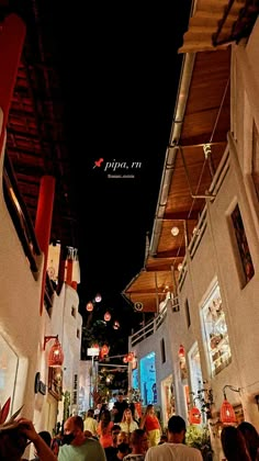 people sitting at tables in an alleyway with lights hanging from the ceiling above them