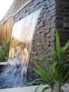 a waterfall is shown in front of a brick wall and green plants with water coming from it