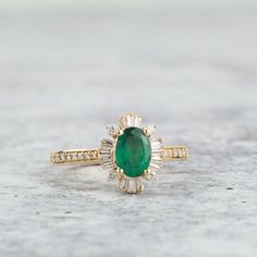 an emerald and diamond ring sitting on top of a stone surface with white diamonds around it