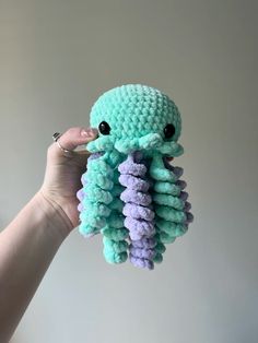 a hand holding up a crocheted stuffed animal with purple and green tentacles on it