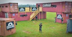 a man standing in the middle of a field next to red shipping containers and stairs