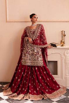 a woman in a red lehenga standing next to a white table and fireplace