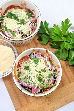 two bowls filled with food sitting on top of a wooden cutting board next to parmesan cheese