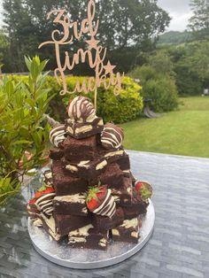 a cake with strawberries and chocolate on top sitting on a table in front of some bushes