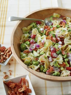 a wooden bowl filled with pasta salad next to other dishes and utensils on a table