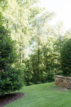 a stone bench sitting in the middle of a lush green park with lots of trees