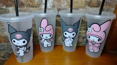 four plastic cups with cartoon characters on them sitting on a wooden table next to a brick wall