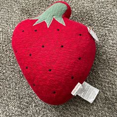 a red strawberry shaped pillow on the floor with a tag hanging from it's side