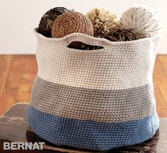 a crocheted basket with yarn and pine cones in it on top of a wooden table