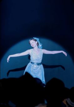 a woman in a blue dress is dancing on stage with her arms spread out to the side