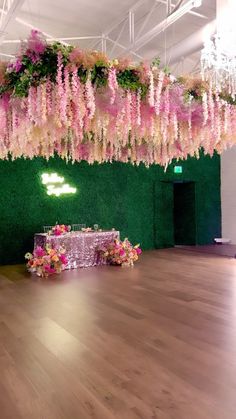 a room filled with lots of pink flowers and greenery hanging from the ceiling over a table