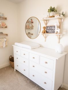 a baby's room with white dressers and shelves on the wall above it