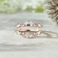 a rose gold wedding ring with pear shaped diamonds on the side, sitting next to a cactus