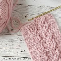 a pink crochet blanket next to a ball of yarn and a knitting needle