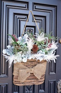 a basket filled with white flowers and greenery hanging from a door handle on a black front door