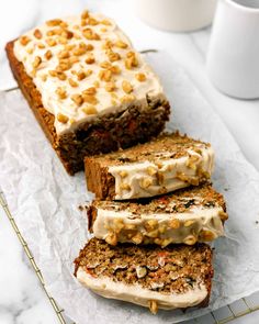 three slices of carrot cake with cream cheese frosting and nuts on top, next to a cup of coffee