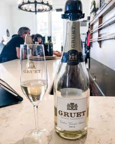 a bottle of wine sitting next to a glass on a table with people in the background