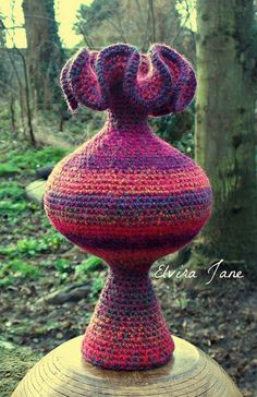 a crocheted vase sitting on top of a wooden stump in the woods with trees behind it