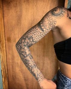 a woman with a tattoo on her arm standing in front of a wooden paneled wall