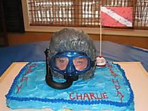 a cake with a scuba theme on it and a person wearing a diving mask sitting in front of the cake