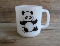 a white coffee cup with a black and white panda bear on the front, sitting on a wooden surface