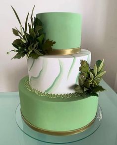 a three tiered cake with green and white designs on it, sitting on a glass table