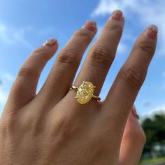 a woman's hand with a yellow diamond ring on her finger, against a blue sky