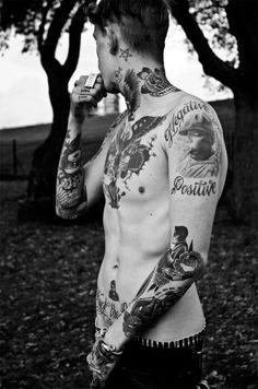 black and white photograph of a man with tattoos on his body drinking from a bottle