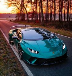 a blue sports car parked on the side of the road near trees and water at sunset