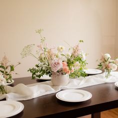 the table is set with white plates and flowers