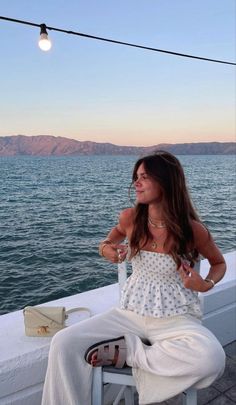 a woman sitting on top of a white chair next to the ocean with a light bulb above her head