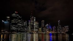 the city is lit up at night and reflecting in the water