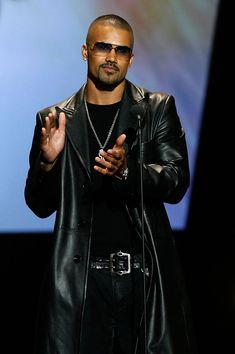 a man in a black leather jacket is holding his hands up while standing on stage