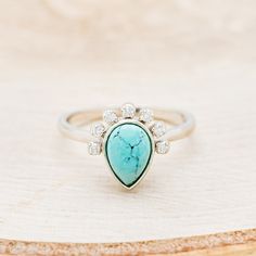 a turquoise stone and diamond ring sitting on top of a piece of wood with a white background