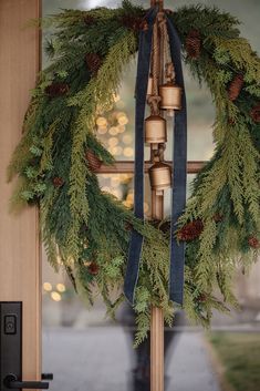 a wreath with bells and pine cones hanging from it's side on a door