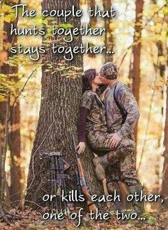 a couple kissing in the woods next to a tree with their hunting gear on it