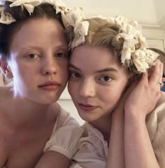 two women with flower crowns on their heads are posing for the camera, both wearing white dresses