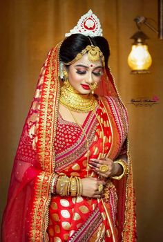 a woman in a red and gold bridal outfit with her hands on her chest