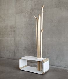 a white shelf with two wooden sticks on it and a vase next to it in front of a concrete wall