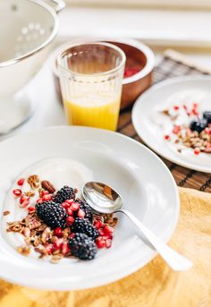 a plate with granola and berries on it next to a bowl of orange juice