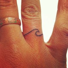 a close up of a person's hand with a tattoo on their ring finger