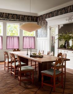 a dining room table surrounded by chairs and windows with pink curtains on the window sill