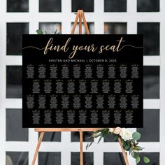 a black and white wedding seating sign with greenery on it that says find your seat