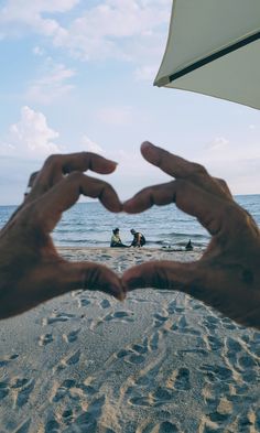 two hands making a heart shape on the beach