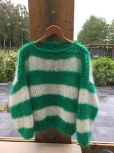 a green and white sweater hanging on a wooden hanger in front of a window