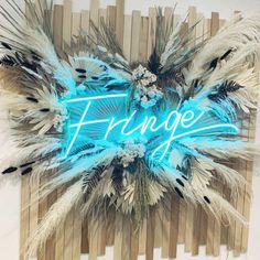 a blue neon sign that says fringe on top of some wood sticks with feathers around it