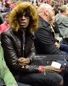 a man wearing sunglasses and a fur hood sits in the stands