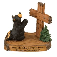 a statue of a bear sitting in front of a wooden cross with the words when life makes it easy to stand, get on your knees & pray