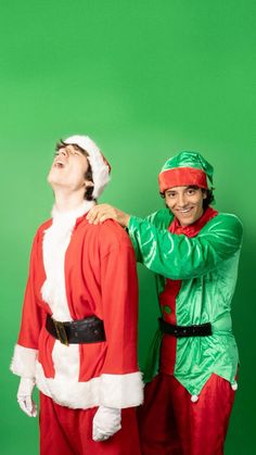 two men dressed as santa clause and elfs are posing for a photo in front of a green background